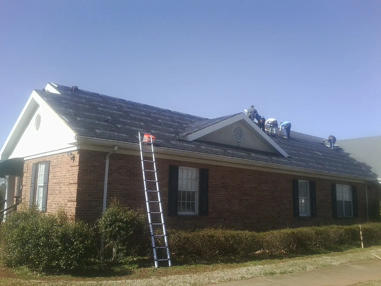 Crew tearing shingles off a brick ranch roof with a ladder set — Metal Roof Repair work by our crew in Streator