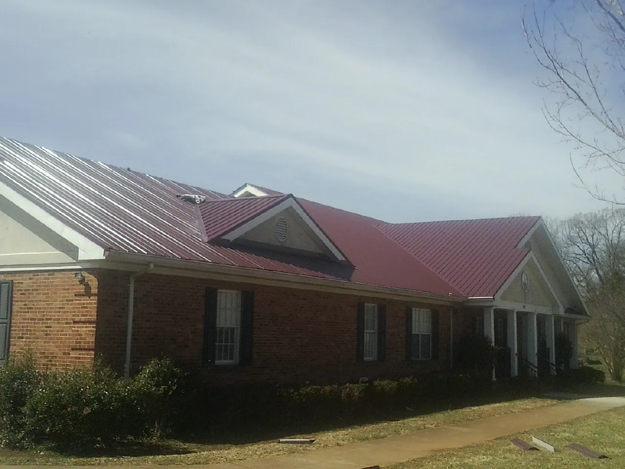 Red metal roof with gabled entries on a long brick building, from a Hail Damage Roof Repair job in Streator