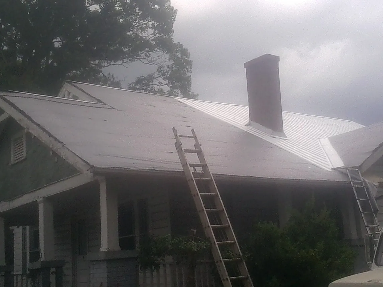 Ladders against a metal roof on an older home with a brick chimney in Streator