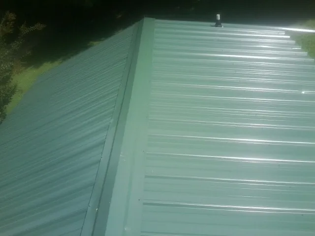 New green metal panels meeting at the ridge of a roof — Flat Roof Repair work by our crew in Streator