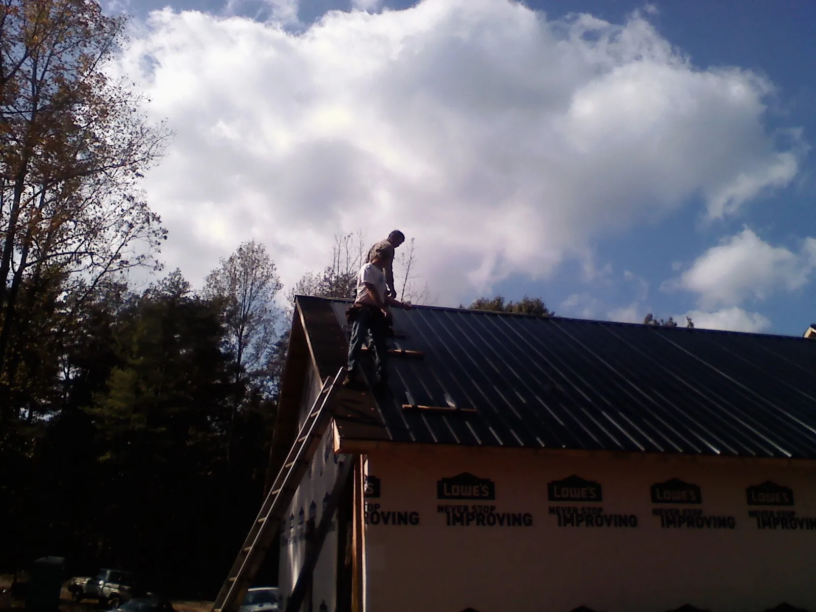 Roofer fastening dark metal panels high against a cloudy sky, from a Roof Inspection job in Streator