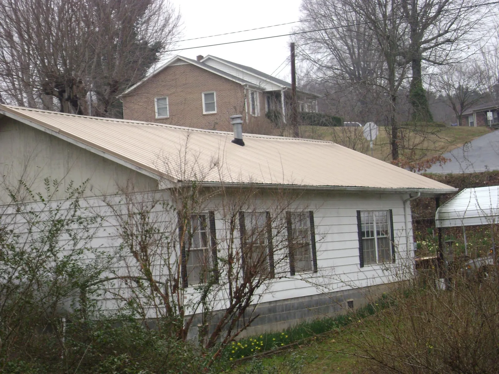 Tan metal roof on a white sided house set into a hillside — Commercial Roofing by Roofing Brothers in Streator